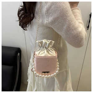 Detail of a pink drawstring bucket bag with pearl handle and golden chain on a model
