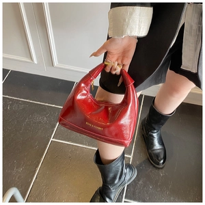 Detail of red patent leather dumpling bag with gold lettering and metallic handle