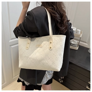 Detail of cream-white tote bag showing quilted texture and logo plate on a model's shoulder