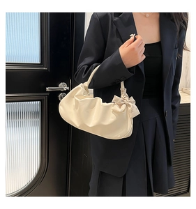 Detail of a creamy white pleated cloud bag with a silk scarf accent on a model's shoulder