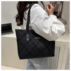 Detail of black embossed tote bag with gold brand plaque and glittery texture on shoulder strap