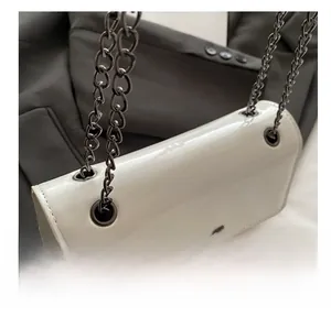 Detail of white glossy patent leather square bag with metal eyelets and black chain strap