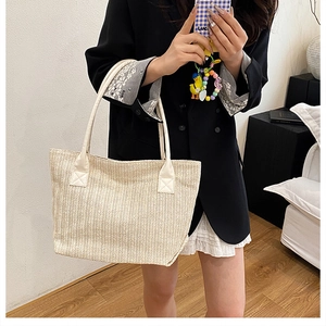 Detailed herringbone texture of a beige woven tote bag with white canvas handles