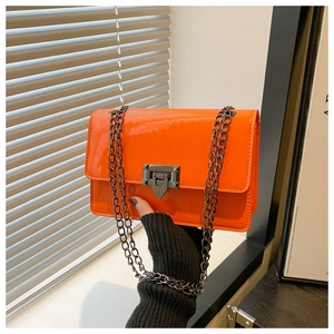 Macro shot of bright orange patent leather crossbody bag with metallic chain and stud buckle