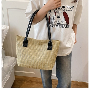 Detail of cross-stitched reinforced handles on a woven straw tote bag for beach vacations