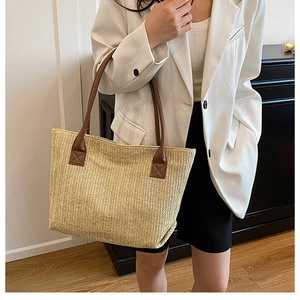 Detail of woven straw tote bag featuring brown leather shoulder straps and V-shaped texture