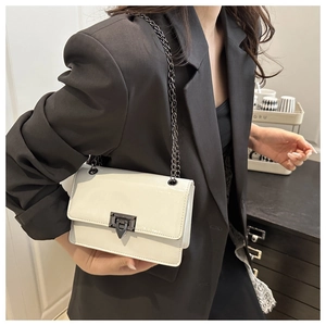 Detail of a creamy white glossy patent leather crossbody bag with a dark metal buckle