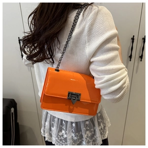 Detail of orange patent leather crossbody bag with chain strap worn by a model