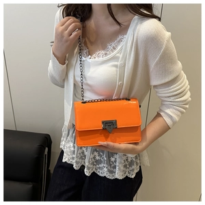 Detail shot of orange patent leather crossbody bag with black chain strap on a person