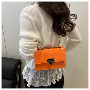 Detail of vibrant orange patent leather crossbody bag with black chain and metal lock clasp