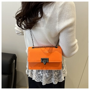 Detail of bright orange patent leather crossbody bag with black geometric clasp on model