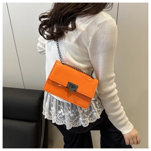 Detail of bright orange patent leather crossbody bag with arrow metal clasp on white sweater