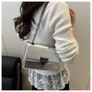 Detail of silver metallic shoulder bag with metal twist lock and chain strap on model