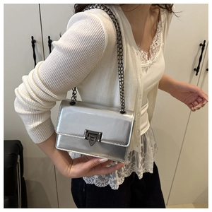 Detail of silver metallic crossbody bag with chain strap and stylish clasp on a model