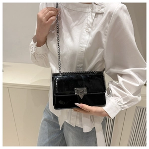 Detail of glossy black patent leather square bag with V-shaped metal lock and chain strap