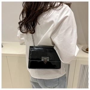 Detail of glossy black patent leather shoulder bag with silver metal chain and geometric clasp