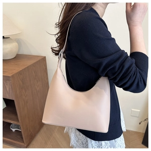 Close-up of minimalist beige hobo bag worn on shoulder over navy blue sweater