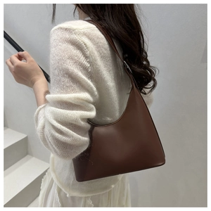 Minimalist dark brown leather shoulder bag shown under the arm on white knit sweater