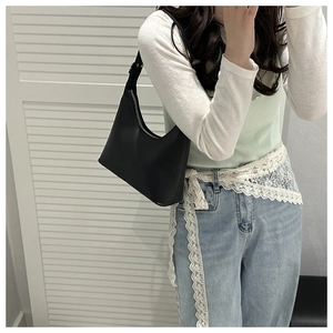 Close-up of a minimalist black hobo underarm bag worn by a model in a white setting