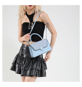 Light blue leather handbag with oval metal buckle shown with a black outfit in a studio