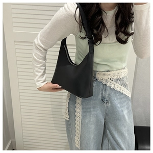 Close-up of minimalist black matte hobo bag with silver buckle worn on shoulder