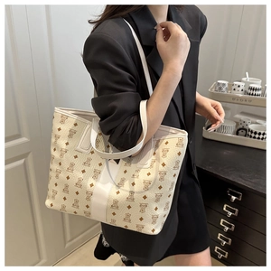 Détail d'un grand sac cabas crème à motif d'ours et bandoulière en cuir porté sur un blazer noir