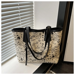 Close-up of woven cream tote bag featuring black graffiti patterns and leather straps