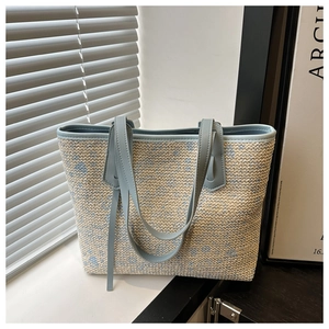 Detail of woven straw tote bag featuring blue floral patterns and light blue leather straps