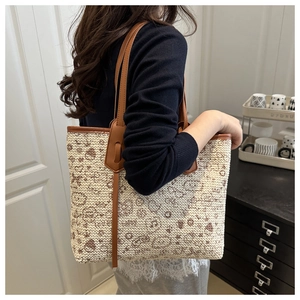 Detail of woven straw tote bag with brown leather straps and character pattern