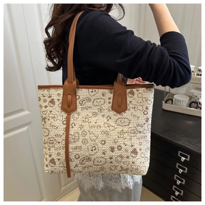 Detail of woven tote bag with brown leather strap worn over shoulder in modern interior