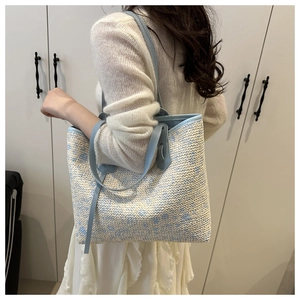 Detail of blue floral straw tote bag with leather straps on a model in a minimal setting