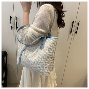 Detail of woven straw tote bag with blue floral patterns and leather trim accents