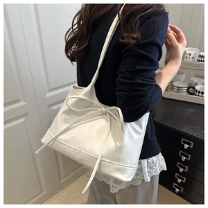 Detailed view of a white tote bag featuring a decorative bow knot and matte leather finish