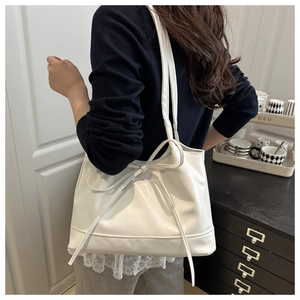 Detail view of cream white bow tote bag worn by model in an elegant interior setting
