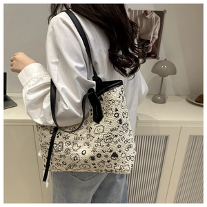 Detail of a large cream woven tote bag with black graffiti doodles and leather handles