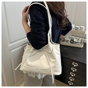 Detail of a white oversized tote bag with decorative bow and sleek shoulder straps