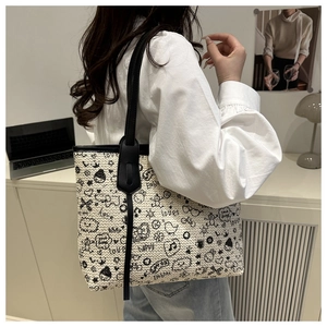 Close-up of beige woven tote bag with black graffiti prints worn by a model in a modern office