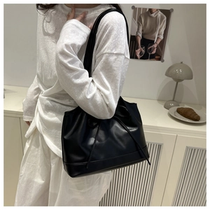 Detail of a black pleated tote bag with a bow accent and long shoulder straps