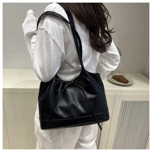 Detail of black leather tote bag featuring a bow decoration and reinforced bottom edge