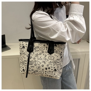 Detail of a large woven tote bag with black graffiti prints and leather handles on a model