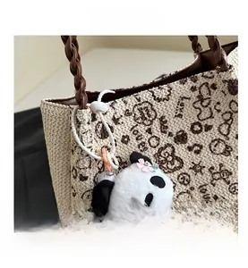Détail d'un sac cabas tissé beige avec anses en cuir marron et pendentif panda