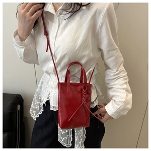 Mini cabas en cuir rouge brillant avec bandoulière porté par un mannequin en style urbain