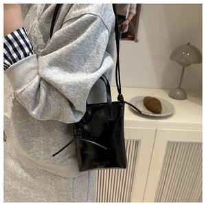 Détail d'un petit sac de téléphone noir brillant avec inscription et bandoulière nouée