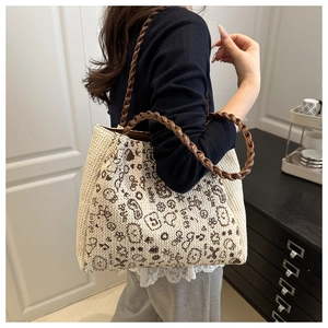 Detail of a beige woven tote bag with cartoon prints and brown leather handles