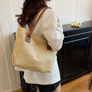 Large khaki woven tote bag with brown leather handles worn by model in a minimal setting