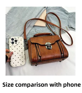 Mini vintage brown leather handbag with silver lock and adjustable strap beside a phone