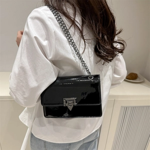 Minimalist black patent leather crossbody bag with metal chain strap on a white shirt