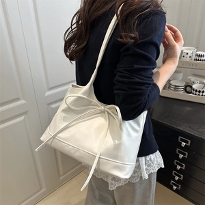 White shoulder tote bag with a large bow detail shown on model in a cozy indoor setting
