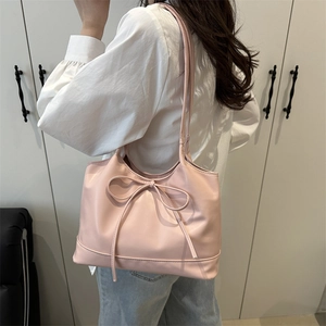 Pink faux leather tote bag with bow detail shown from a side view on female model
