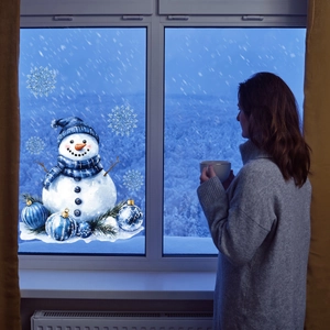 Cozy winter scene showing a snowman window sticker with a woman looking at snowy view